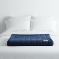 Nocturely Weighted Blanket in deep navy blue waffle texture on a minimalist white bed